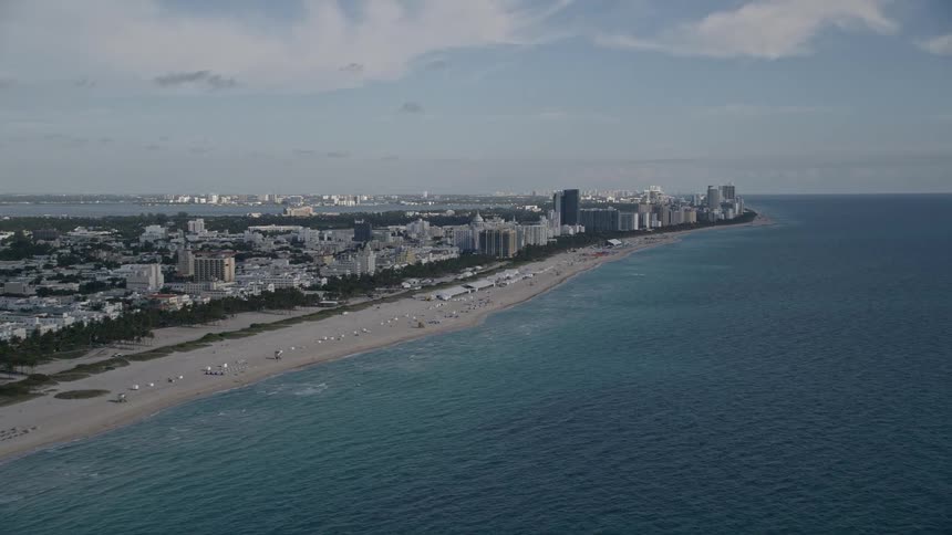 Aerial footage panning right from South Beach to Miami Beach showcasing the popular destinations shoreline filled with sunbathers and beachgoers during a partly cloudy day
