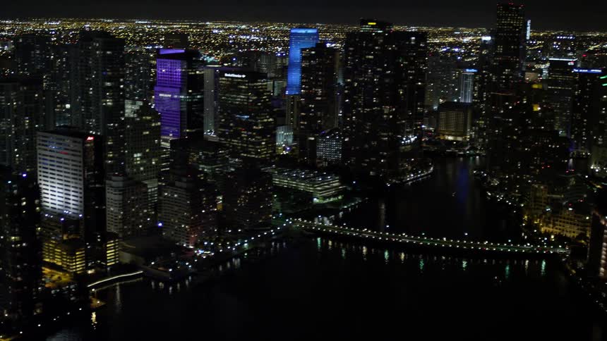 Pan across Downtown Miami skyscrapers at night capturing the citys metropolis clear skies shoreline and small bridges