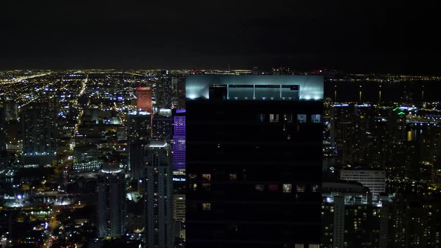 Approaching and orbiting the Four Season Hotel tower at night in Downtown Miami surrounded by clear skies and city lights