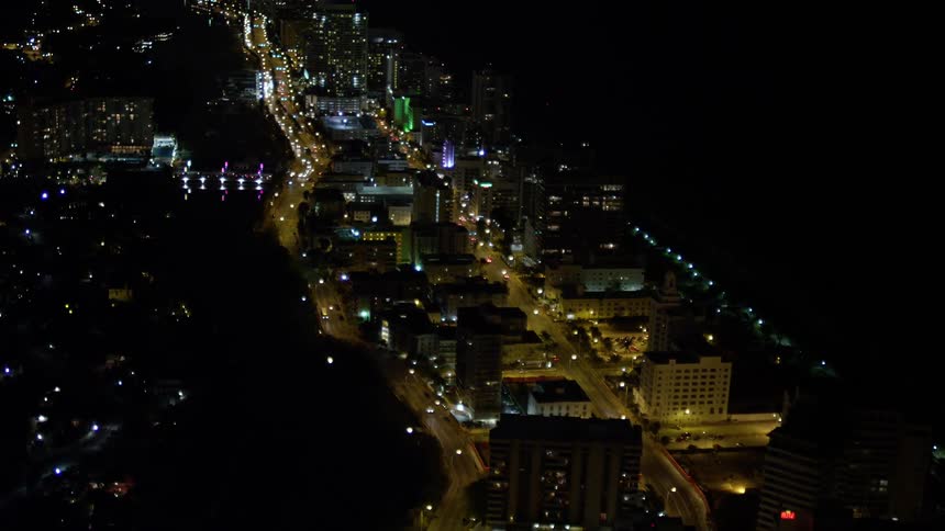 Fly over Miami Beach streets at night tilting up to approach an illuminated resort hotel for a stunning aerial view