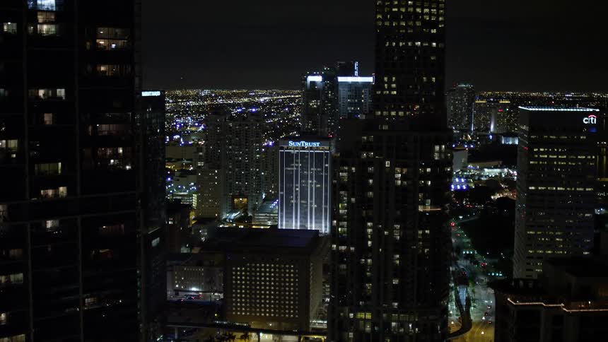 A breathtaking aerial view from a bridge over the waterway revealing and approaching the superstructures of skyscrapers in Downtown Miami at night in Florida