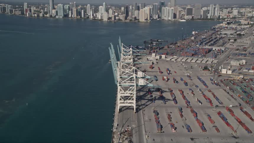 Aerial footage of cargo cranes and containers in Port of Miami revealing Downtown Miamis high rise skyline and waterfront industrial area