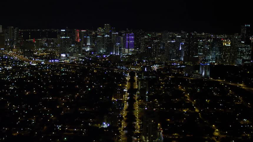 A breathtaking aerial tilt up video of the colorful downtown Miami skyline at night with numerous high rise buildings illuminated beautifully