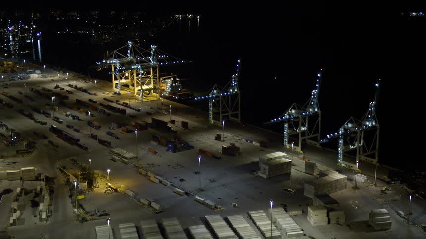 An aerial approach to cargo cranes and ships at the Port of Miami during a clear night