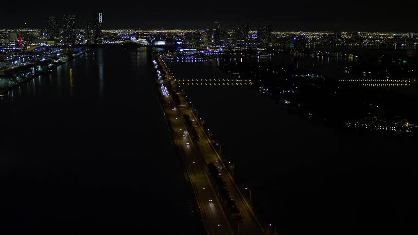 A nighttime aerial view of the MacArthur Causeway showcasing light traffic revealing the coastal shoreline in Miami Florida