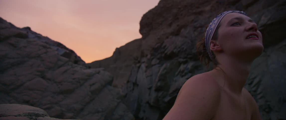 A young woman sitting outside surrounded by large rocks behind her