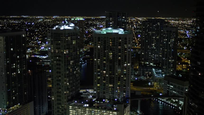 A nighttime aerial view of downtown Miami along the Miami River passing skyscrapers and high rises in southern Florida