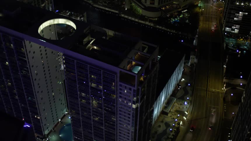 Approaching 500 Brickell tilt down to rooftop pool overlooking Downtown Miamis metropolis at night