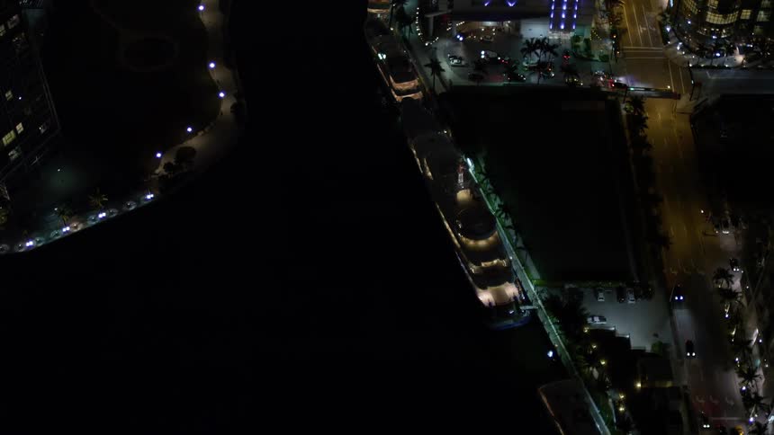 A 5k aerial footage of a yacht gliding along the river with Downtown Miamis towering skyscrapers in the background shot at nighttime in Florida
