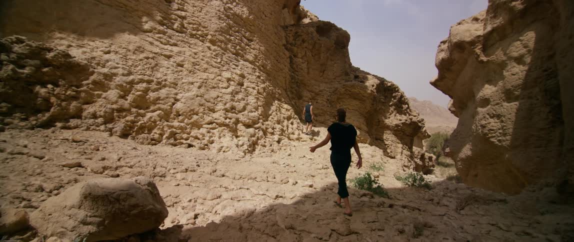 Man waits for woman near cliff before they hike along the rough uneven ground