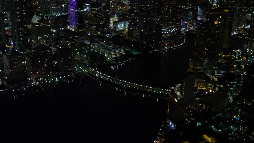 A breathtaking 5k aerial view of the skyline of Downtown Miami Florida at night including the Brickell Key Drive Bridge over a waterway reflecting the lights