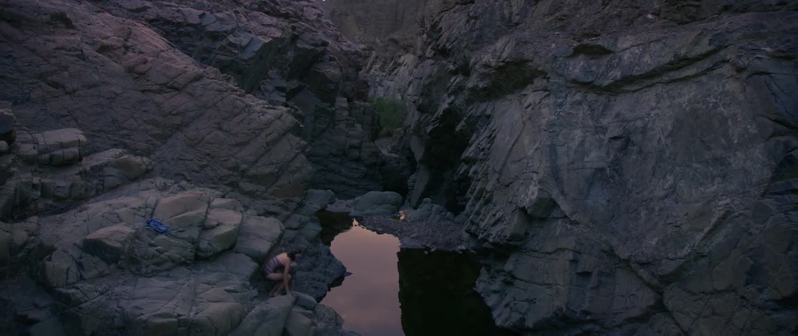 A woman climbing down a rock towards a creek at dusk