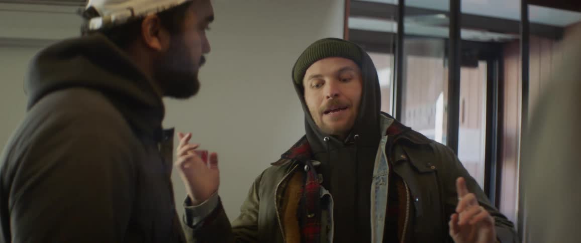 Two men talk in a room with a large glass door
