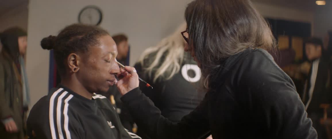Woman puts makeup on another woman while another woman watches