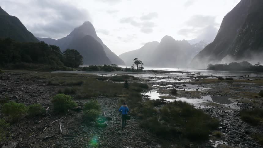 Two people walk along the shore surrounded by hills