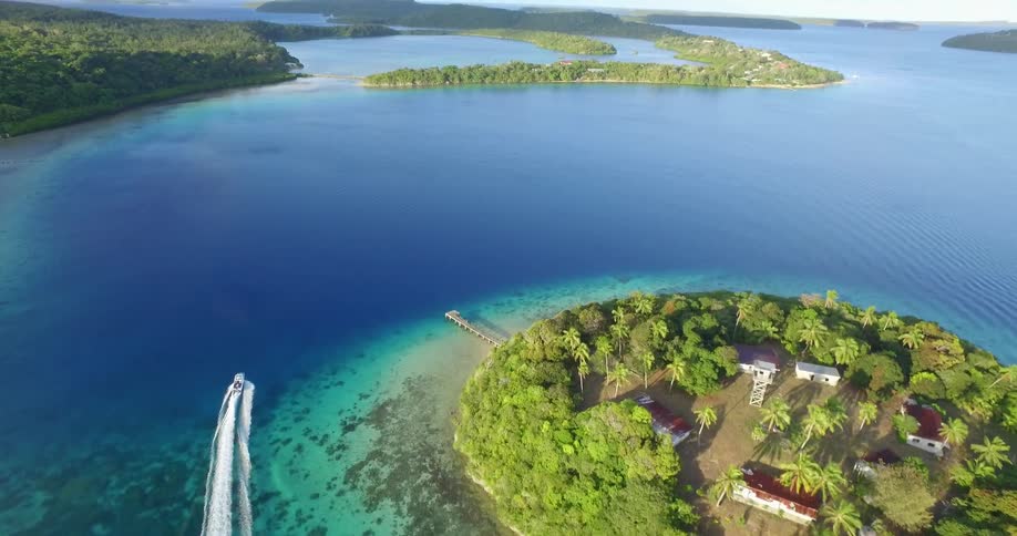 A boat traveling around an island in a large body of clear blue water
