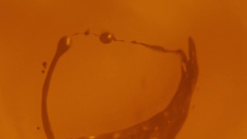 A small amount of reddish orange liquid is vibrated as it swirls