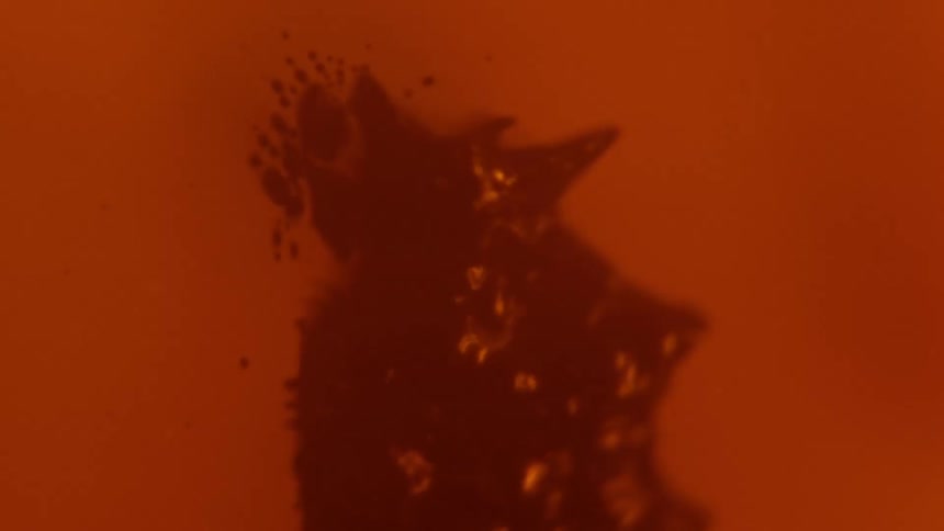 A thick red organic substance curls as it moves and splashes and splatters in a pulsating manner