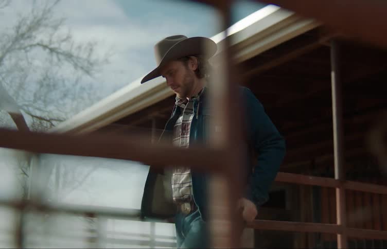 Man wearing cowboy hat walks away from building and brushes off his jacket