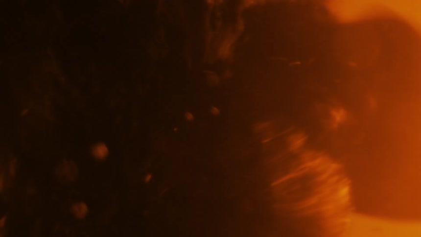 Dark mass containing particles expands and shakes in orange liquid