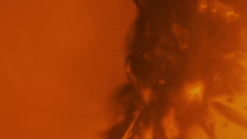 A thick red substance spins and splatters as droplets fly as it moves in an orange liquid atmosphere