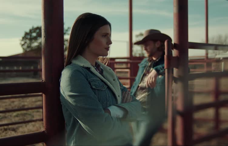 People lean against corral fence and turn to face each other