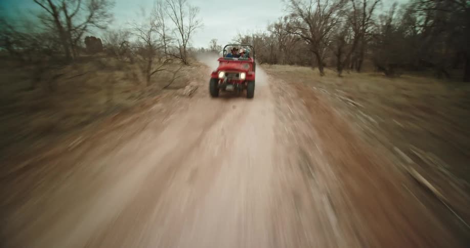 A jeep rides down a dirt road through barren forest