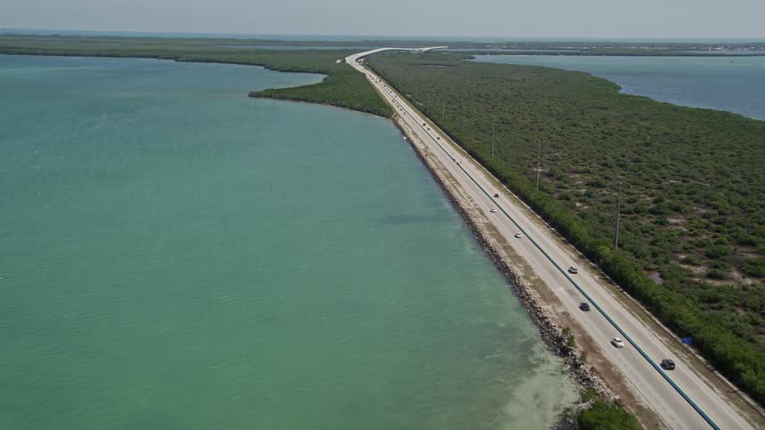 Aerial view of light traffic on Overseas Highway in Key Largo passing through a forested strip of land and surrounded by water