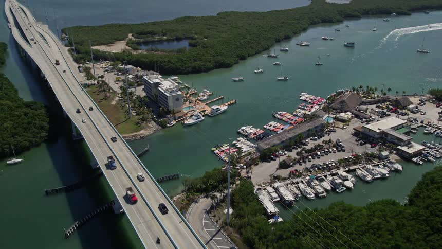 Aerial view of traffic moving over the scenic Overseas Highway with boats parked in a marina and sailing in the water passing by the luxurious Anchorage Resort and Yacht Club and the popular Gilberts Resort in Key Largo Florida