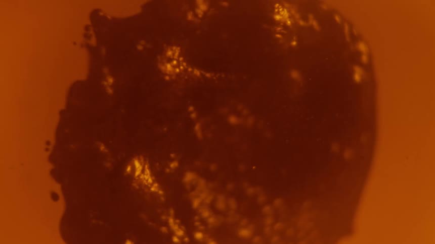 A close up of a red fluid blob moving around slowly in liquid
