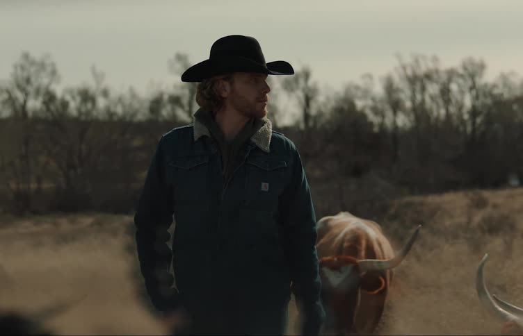 A man stands with his cattle in a field