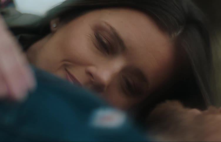 Couple lies on their backs outdoors and the woman briefly smiles at the man
