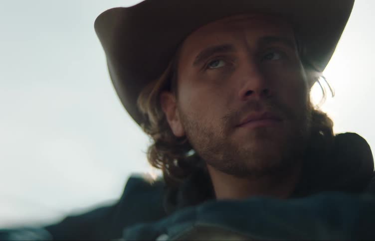 A man in a cowboy hat looks off into the distance while outdoors
