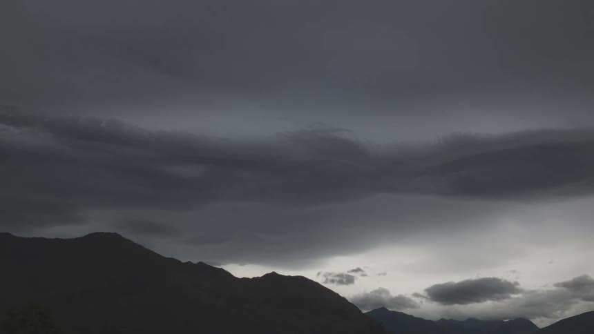 Landscape of mountains being silhouetted agains the sky with floating gray clouds