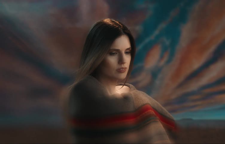 Woman wraps herself in a striped blanket while posing against scenic photography backdrop outdoors