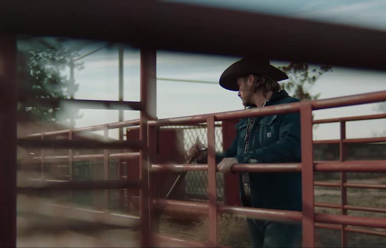 A man is leaning his arms on a fence gate and he pulls it closed and walks away