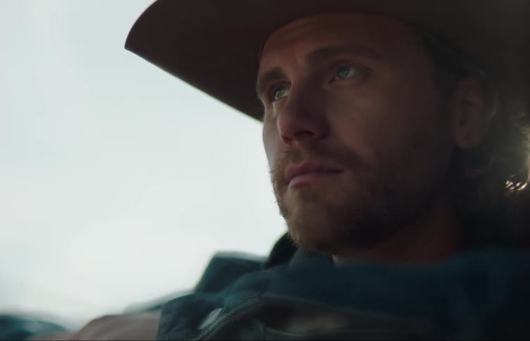 A man in a cowboy hat leans against a railing