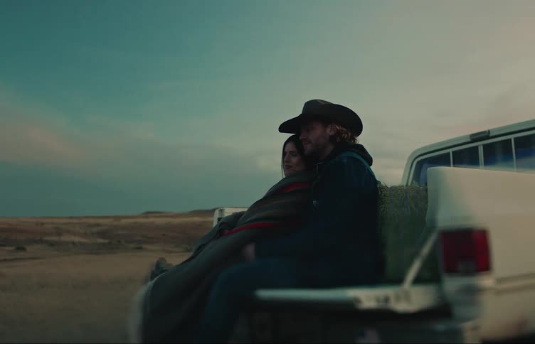 A man and woman sitting on the bed of a truck cuddling one another leaning against hay