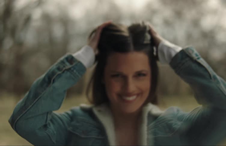 A woman is outside laughing and spinning while playing with her hair