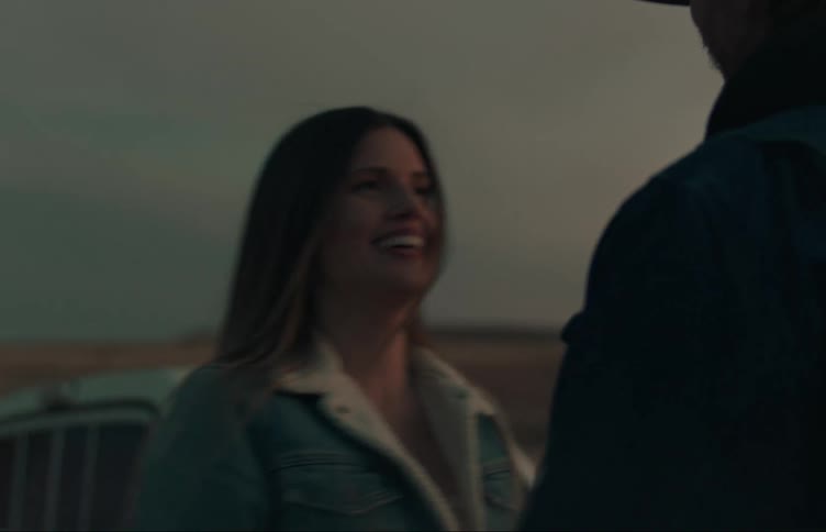 A man and woman stand outdoors and then hold hands while walking