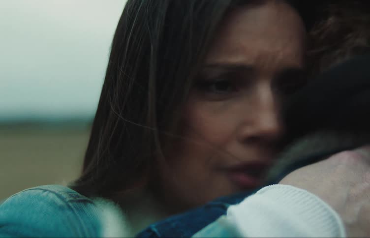 A woman cries while hugging her partner in a field