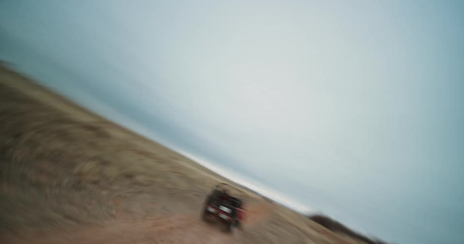 A drone view of a red jeep driving on a dirt road in the desert on a cloudy day