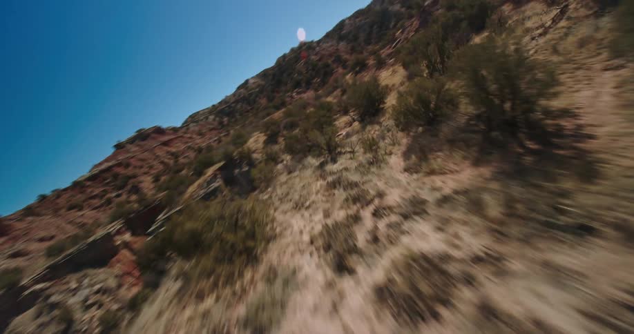 Scrub fills uneven land between hills and mesa bordering ravine on sunny day