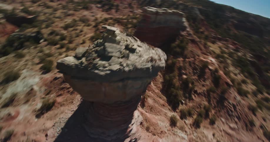 The sun shines upon a tall rock formation in the desert badlands under a clear blue sky