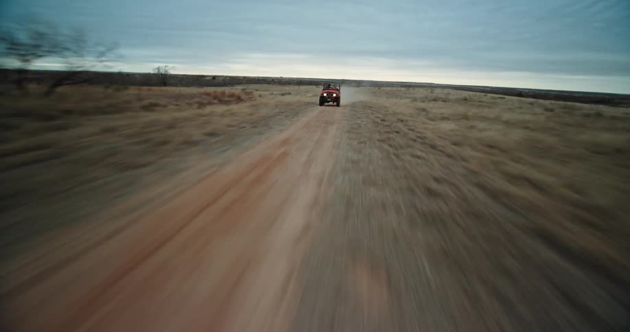 Intense fast aerial view of a red jeep driving on a road in the desert at daytime