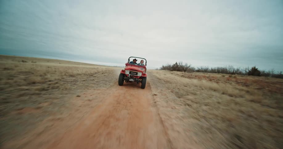 A man and woman riding in a red jeep driving it across desert roads