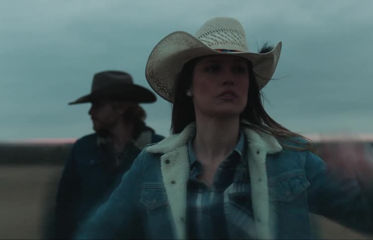 Woman and man in cowboy hats and denim jackets stand in the field at dusk