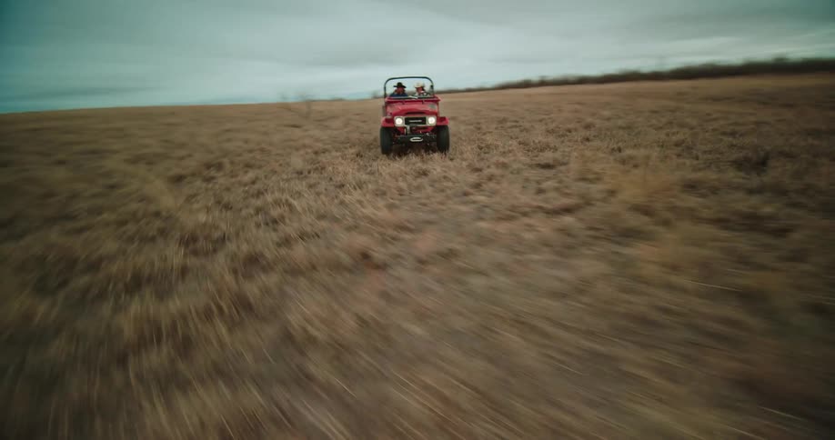 Twisting aerial view of a red jeep driving on a road in the desert at daytime