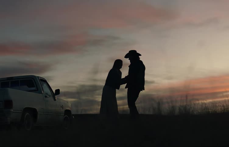 A couple holds hands and then embraces while talking to each other and laughing in front of a sunset