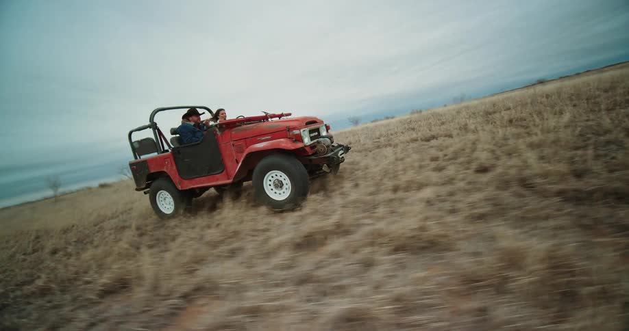 A man and woman ride a jeep through an open field